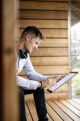 Lächelnder Mann, der ein digitales Tablet benutzt, während er zu Hause sitzt - PESF02206