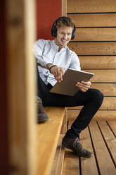 Smiling man wearing headphones using digital tablet while sitting at home - PESF02209