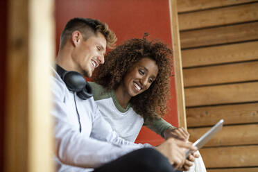 Smiling young couple using digital tablet while sitting at home - PESF02213