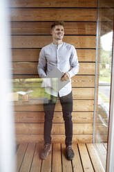 Lächelnder Mann, der ein digitales Tablet hält, während er zu Hause steht - PESF02216