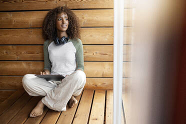 Frau mit digitalem Tablet, die zu Hause im Schneidersitz sitzt - PESF02218