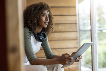 Frau mit Kopfhörer, die zu Hause sitzend ein digitales Tablet benutzt - PESF02225