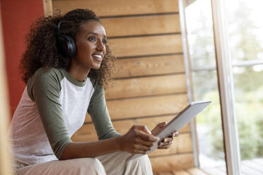 Smiling woman wearing headphone using digital tablet while sitting at home - PESF02226