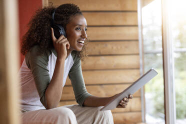 Junge Frau spricht über Kopfhörer, während sie zu Hause ein digitales Tablet benutzt - PESF02227