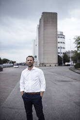 Confident businessman with hands in pockets standing on street - GUSF04740