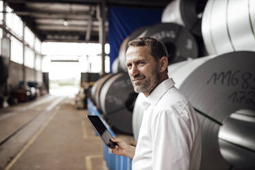 Lächelnder Geschäftsmann mit digitalem Tablet, während er in der Industrie steht - GUSF04744