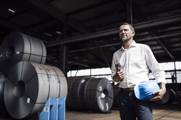 Businessman with digital tablet and hardhat looking away while standing in factory - GUSF04749