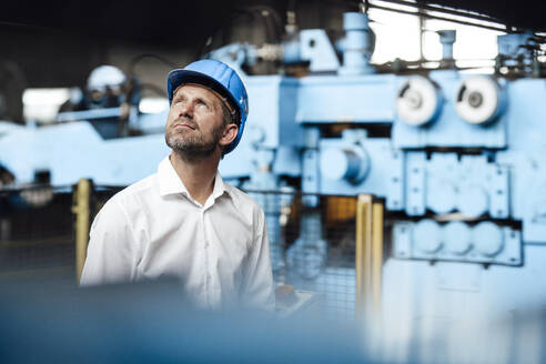 Nachdenklicher männlicher Unternehmer, der in einer Fabrik steht und nach oben schaut - GUSF04824