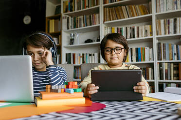 Lächelnder Junge beim E-Learning am Laptop, während ein männlicher Freund zu Hause zuschaut - VABF04034