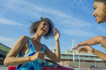 Young woman laughing while looking at female friend in city on sunny day - AJOF00623