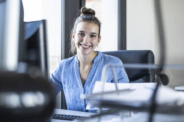 Smiling businesswoman sitting at office - UUF22074