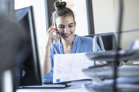 Geschäftsfrau, die im Büro sitzend mit einem Mobiltelefon spricht, lizenzfreies Stockfoto