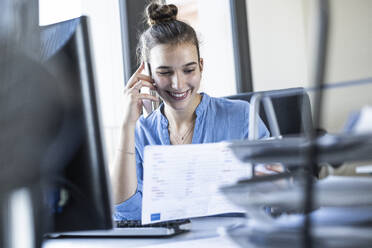 Businesswoman talking on mobile phone while sitting at office - UUF22075