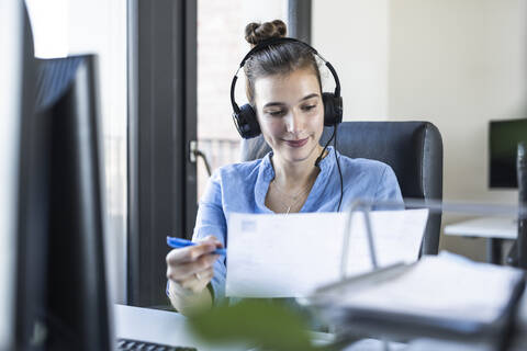 Unternehmer mit Kopfhörern bei der Analyse von Papier während der Arbeit im Büro, lizenzfreies Stockfoto