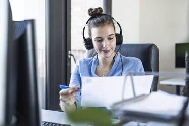 Entrepreneur with headphones analyzing paper while working at office - UUF22080