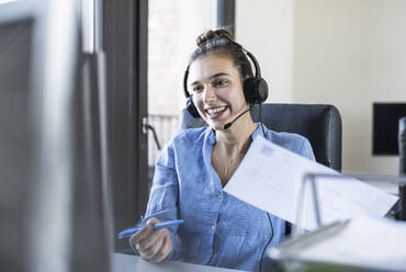 Businesswoman with paper discussing while looking at computer in office  - UUF22083