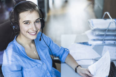 Young businesswoman with headphones and paper working while sitting at office - UUF22086