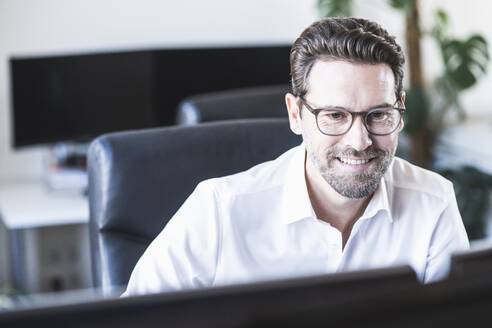 Lächelnder Geschäftsmann bei der Arbeit im Büro - UUF22090