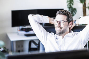 Male entrepreneur sitting with hands behind head at office - UUF22091