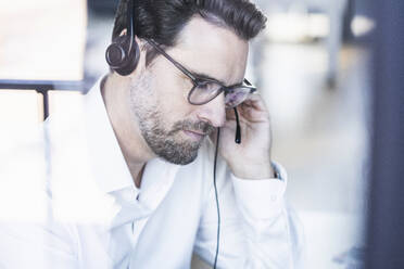 Businessman wearing eyeglasses and headphones working at office - UUF22095