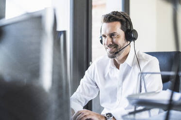 Businessman wearing headphones using computer while sitting at office - UUF22097
