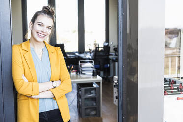 Young businesswoman smiling while standing at entrance in office - UUF22106