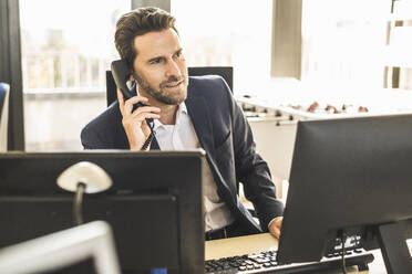 Reifer Geschäftsmann, der im Büro sitzend telefoniert - UUF22122