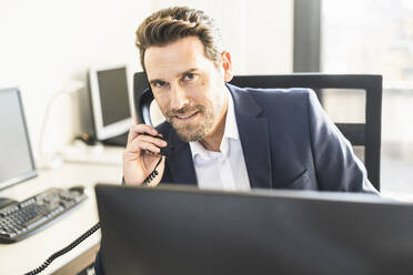 Geschäftsmann lächelnd beim Telefonieren im Büro sitzend - UUF22123