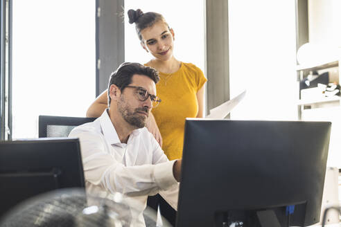 Geschäftsmann und Frau, die einen Computer bei der Arbeit im Büro benutzen - UUF22129