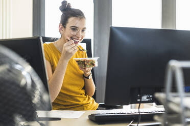 Junge Geschäftsfrau beim Essen in der Mittagspause im Büro - UUF22133