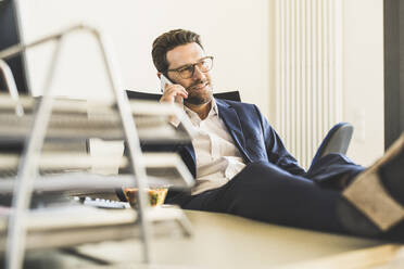Smiling businessman talking on mobile phone while sitting at office - UUF22137
