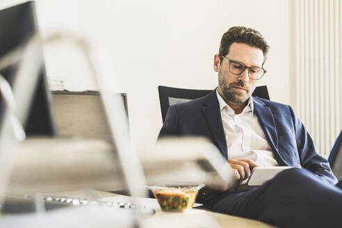 Geschäftsmann, der ein Mobiltelefon benutzt, während er im Büro beim Mittagessen sitzt - UUF22138