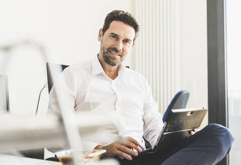 Lächelnder Geschäftsmann mit digitalem Tablet im Büro - UUF22140