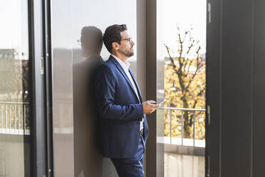 Geschäftsmann, der ein Mobiltelefon benutzt, während er auf dem Balkon eines Büros steht - UUF22141