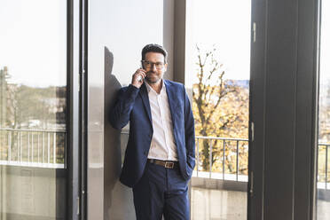 Businessman talking on mobile phone while standing by balcony at office - UUF22143