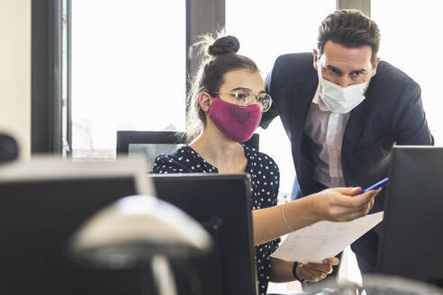 Geschäftsleute mit Gesichtsmaske diskutieren bei der Arbeit im Büro - UUF22147