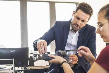 Geschäftsmann, der mit einem Kollegen im Büro einen Quadcopter untersucht - UUF22149