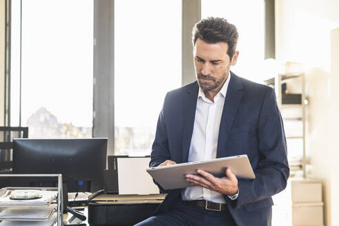 Geschäftsmann im Anzug, der ein digitales Tablet benutzt, während er im Büro sitzt - UUF22152