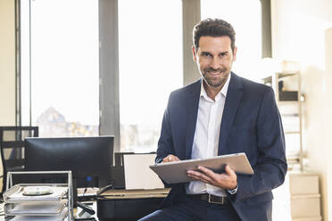 Lächelnder Geschäftsmann, der ein digitales Tablet benutzt, während er im Büro sitzt - UUF22153