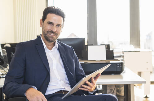 Geschäftsmann lächelnd bei der Verwendung von digitalen Tablet im Büro sitzen - UUF22154