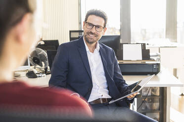 Businessman having discussion with colleague while sitting at office - UUF22155