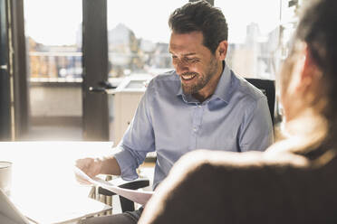 Lächelnder Geschäftsmann, der ein Dokument analysiert, während er mit einem Kollegen im Büro arbeitet - UUF22172
