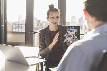 Geschäftsfrau hält Roboter-Spielzeug, während sie mit einem Kollegen im Büro diskutiert - UUF22176
