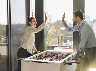 Businessman and woman giving high-five while playing Foosball at office - UUF22183