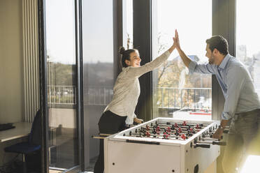 Cheerful business people giving high-five while playing Foosball at office - UUF22184