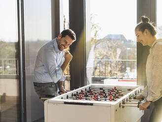 Lächelnder Mann, der eine gewinnende Geste zeigt, während er mit einem Kollegen im Büro Tischfußball spielt - UUF22186