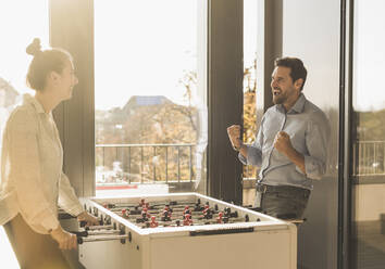 Businessman screaming while playing Foosball with colleague at office - UUF22187