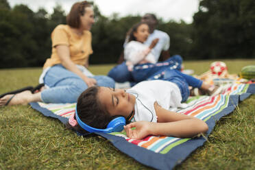 Mädchen mit Kopfhörern, das sich auf einer Picknickdecke entspannt und Musik hört - CAIF30079
