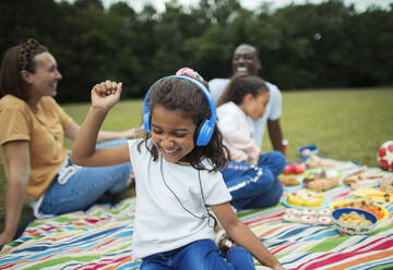 Unbekümmertes Mädchen, das auf einer Picknickdecke mit Kopfhörern Musik hört - CAIF30081