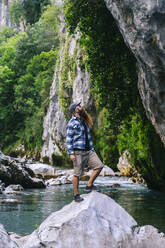 Junger Mann steht auf einem Felsen über einem Fluss beim Wandern im Gebirge Picos De Europa, Asturien, Spanien - DGOF01714